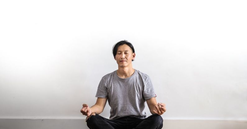 Mindfulness - Photo of Man in Gray T-shirt and Black Jeans on Sitting on Wooden Floor Meditating