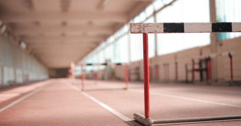 Obstacles - Hurdle painted in white black and red colors placed on empty rubber running track in soft focus
