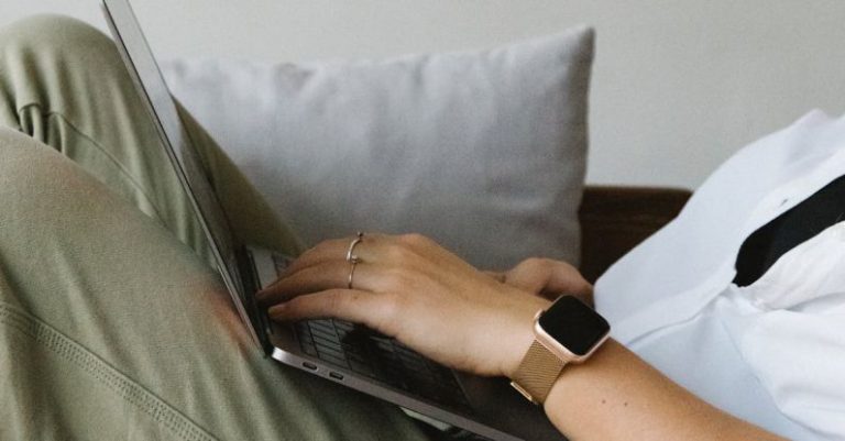 Self-Compassion - Side view of crop unrecognizable female freelancer in casual clothes and smartwatch lying on comfortable sofa and working remotely on laptop